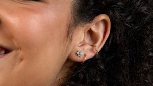 Woman's ear with a conch piercing and first and second lobe piercings with gold jewellery.