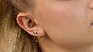 woman with gold and diamond conch piercing, and chain stacked lobe earrings