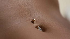 up close of a womans belly piercing with gold jewellery